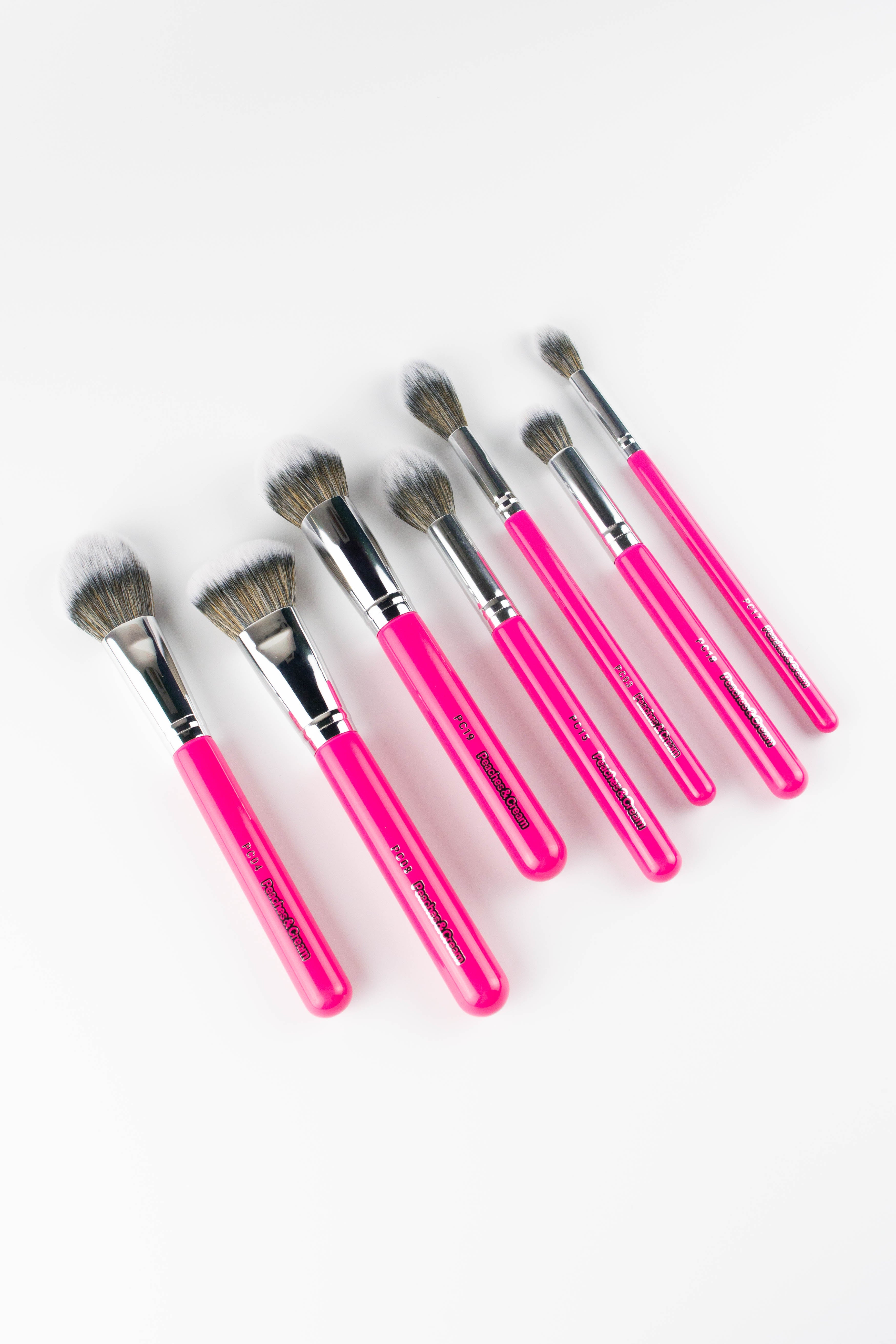 The Peaches and Cream Essential Face Brush Set includes seven face makeup brushes with pink handles, and soft bristles in various shapes and sizes -perfect for flawless application and beautifully displayed on a white background.
