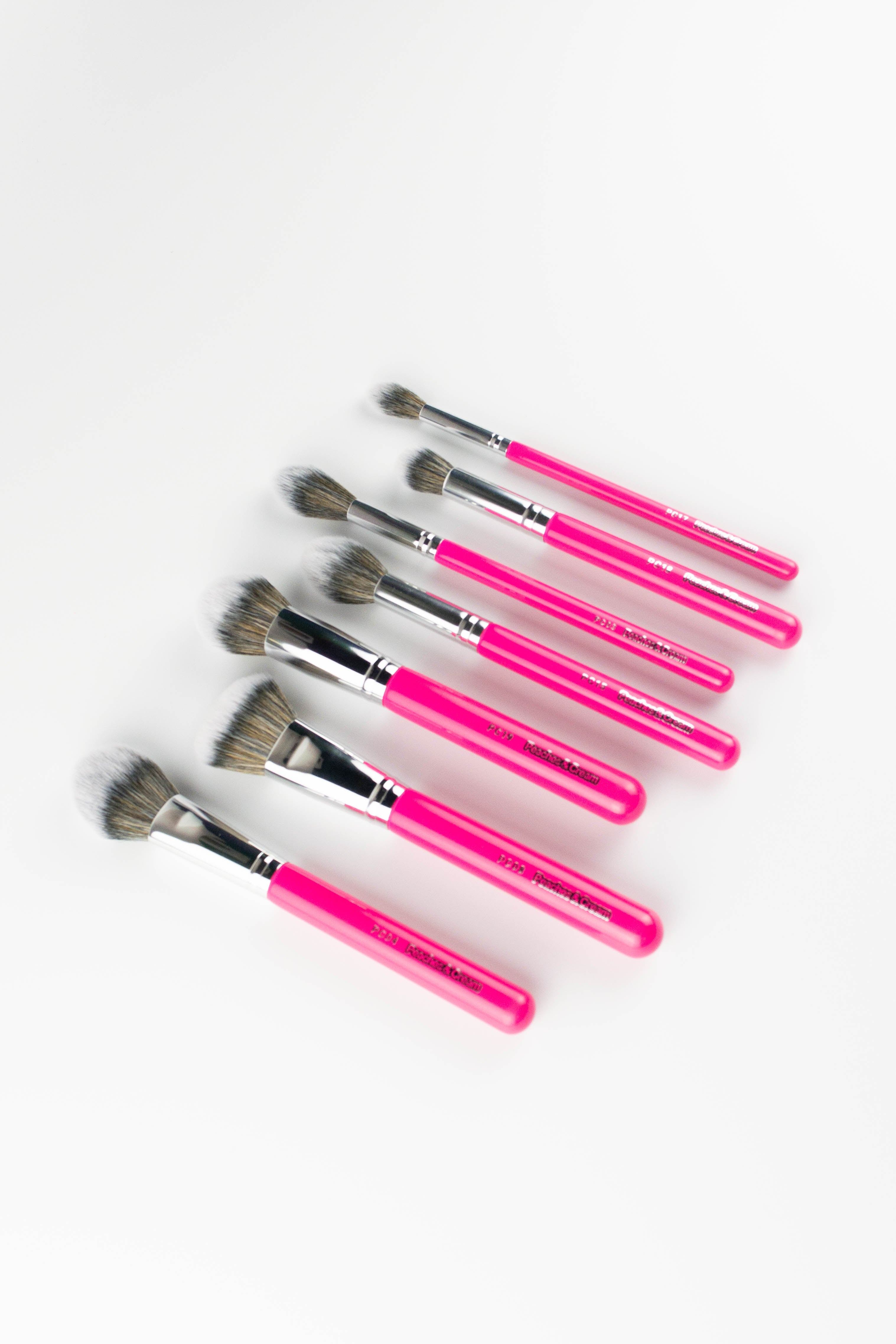 The Peaches and Cream Essential Face Brush Set features seven pink-handled brushes, arranged diagonally on a white background. The set includes various brush sizes and shapes for flawless makeup application.
