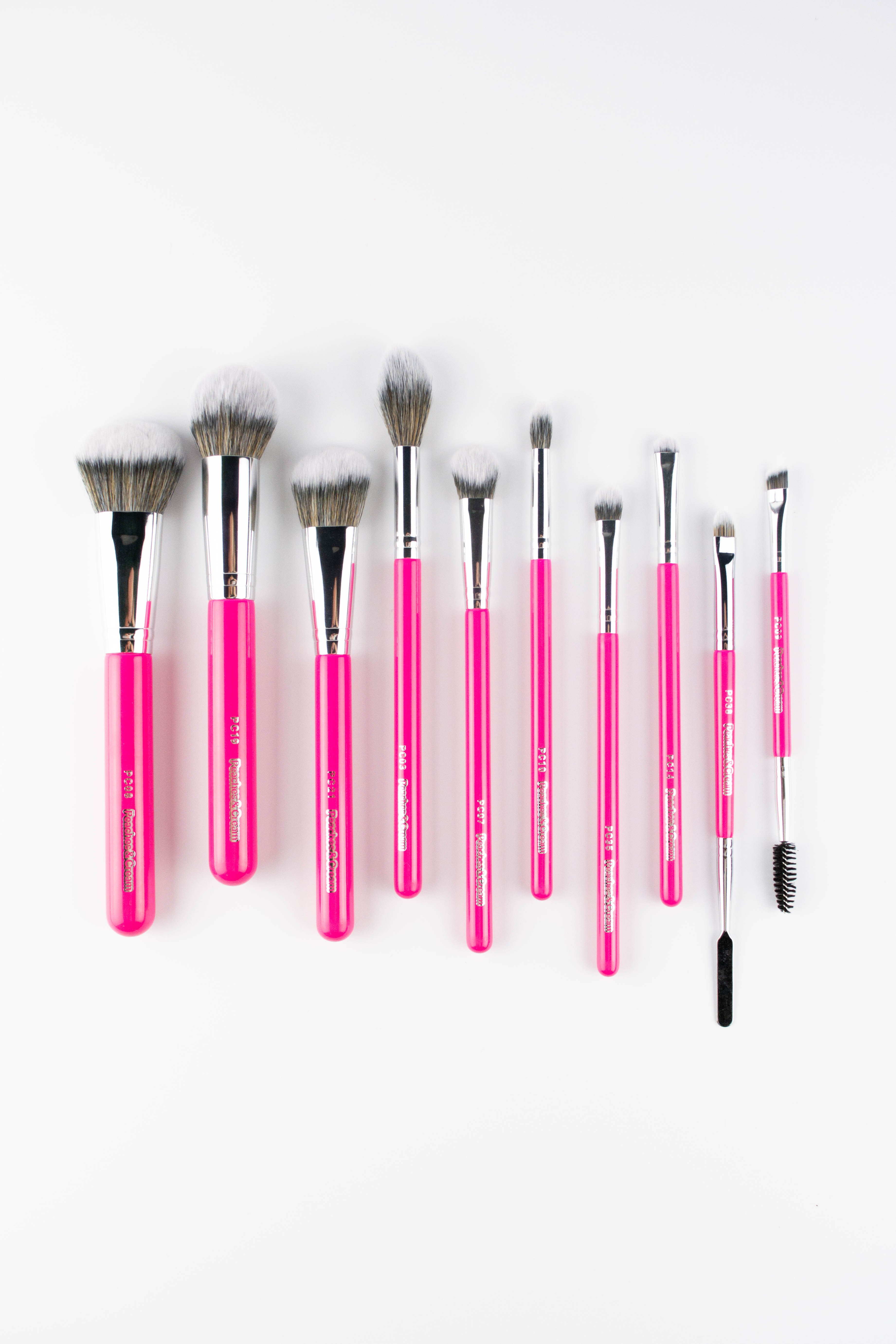 The Top 10 Makeup Brush Set by Peaches & Cream Makeup includes ten pink-handled brushes with soft synthetic fibres, arranged in a row on a white background for flawless makeup application.