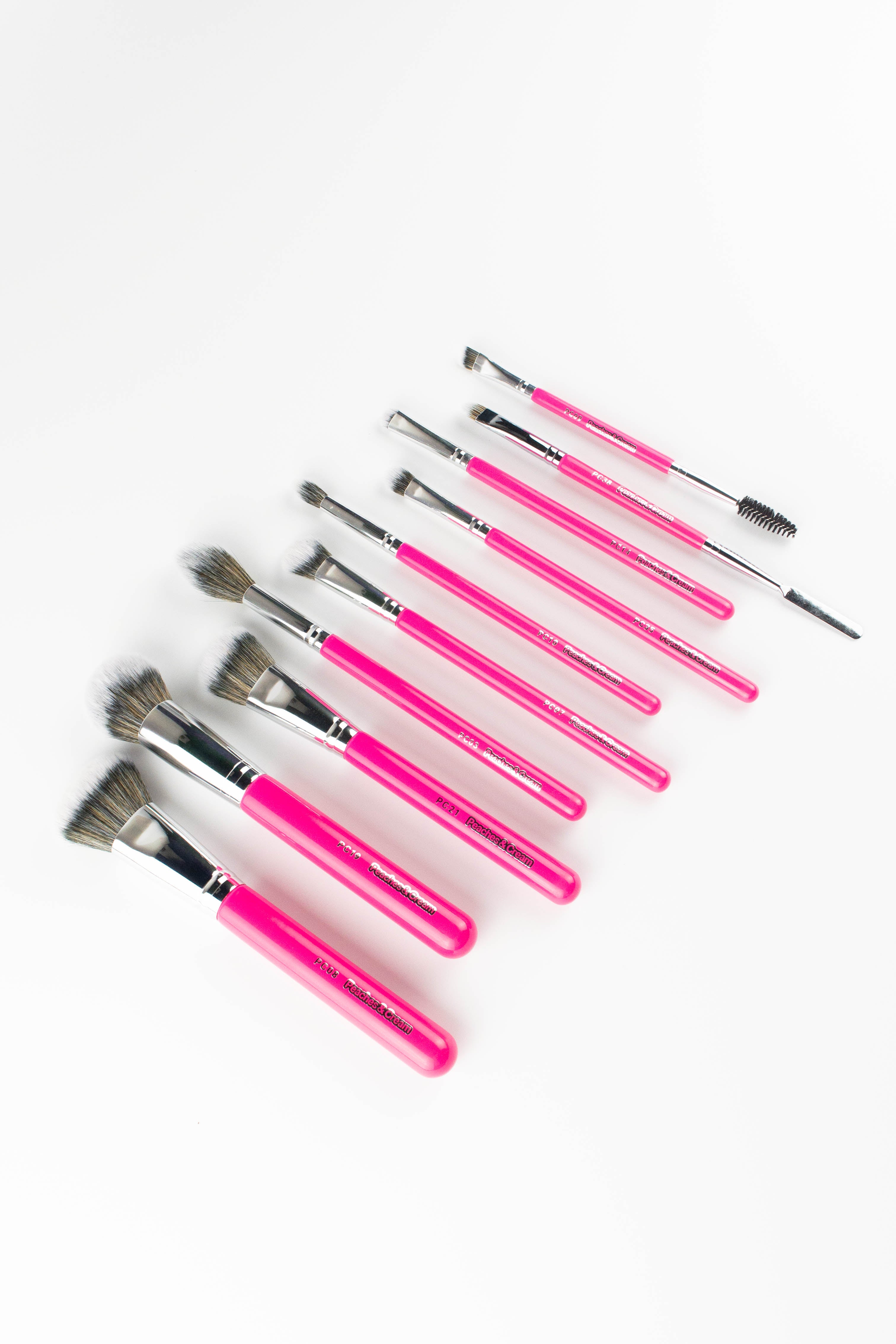 The Top 10 Makeup Brush Set by Peaches & Cream Makeup features ten soft synthetic brushes with bright pink handles and silver ferrules, each designed for different makeup applications. The brushes are displayed diagonally on a white background.