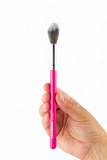 Hand holding a pink pc03 blusher makeup brush with a silver ferrule against a white background by Peaches & Cream 